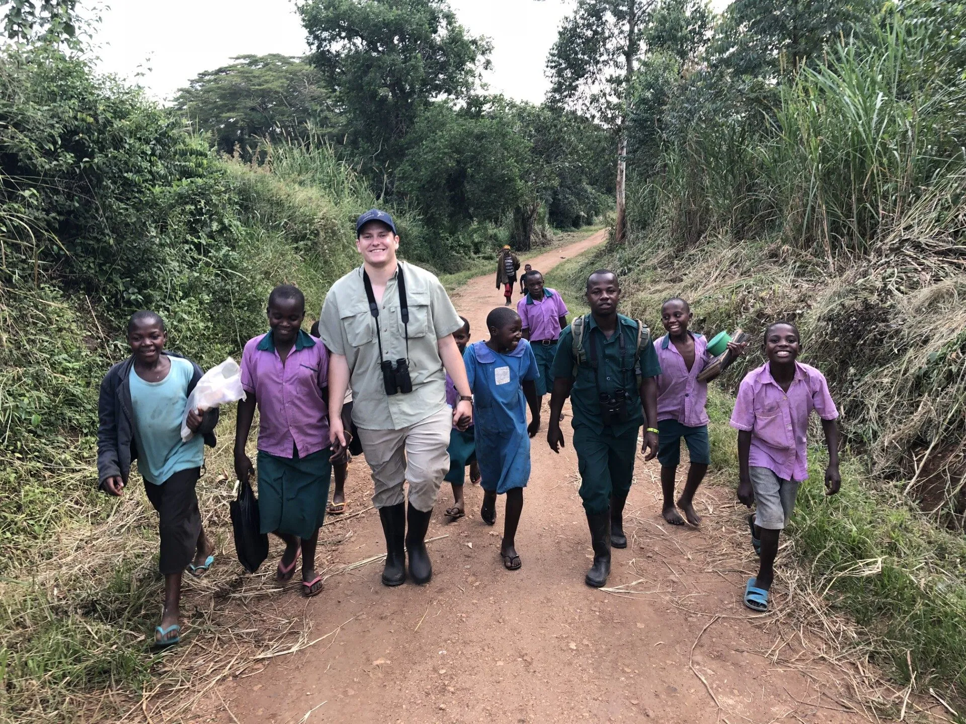 Dan Spears walking down a dirt road with Ugandan schoolchildren